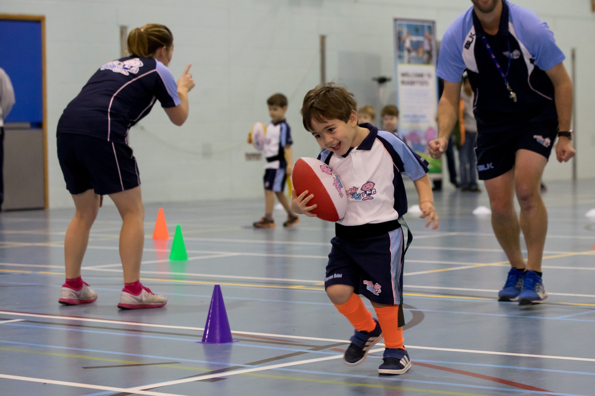 Bambino gioca con il pallone guidato dai coach Rugbytots